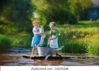 Two cute little girls doing the laundry in a small aluminium basin standing on a pontoon at the pond in a sunny summer day. Kids are playing.
