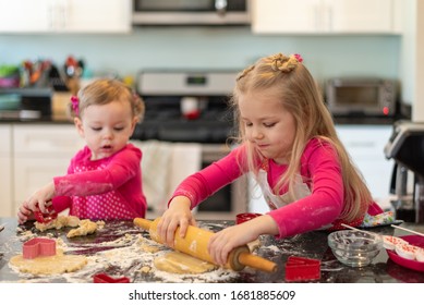 Two Cute Little Girls Rolling Out Dough Making Sugar Cookies On The Kitchen Counter