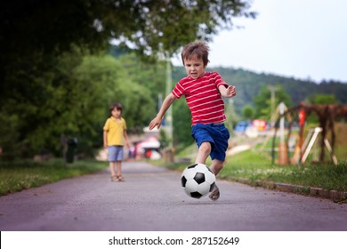 Two cute little kids, playing football together, summertime. Children playing soccer outdoor