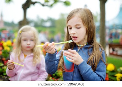 Two Cute Little Sisters Drinking Colorful Frozen Slushie Drink On Hot Summer Day