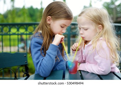 Two Cute Little Sisters Drinking Colorful Frozen Slushie Drink On Hot Summer Day