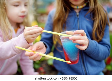 Two Cute Little Sisters Drinking Colorful Frozen Slushie Drink On Hot Summer Day