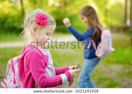 Two cute little sisters playing outdoor mobile game on their smart phones. Modern addictive multiplayer location-based games.
