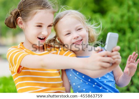 Two cute little sisters playing outdoor mobile game on their smart phones. Kids catching virtual pocket monsters. Modern addictive multiplayer location-based games.