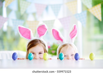 Two Cute Little Sisters Wearing Bunny Ears Playing Egg Hunt On Easter. Adorable Children Celebrate Easter At Home. 