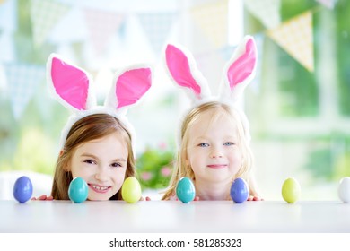 Two Cute Little Sisters Wearing Bunny Ears Playing Egg Hunt On Easter. Adorable Children Celebrate Easter At Home. 