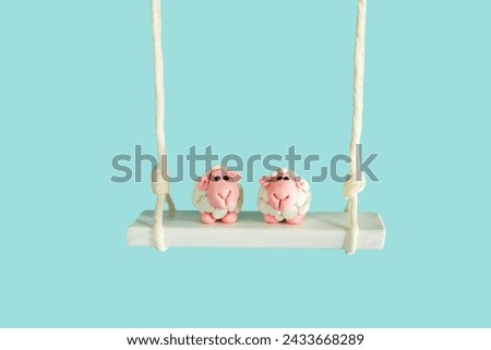 Two cute plasticine sheep are sitting on a swing. Isolated on blue, copy space.