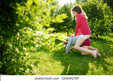 Two Cute Sisters Fooling Around Together On The Grass On A Sunny Summer Day. Children Being Silly And Having Fun. Family Time.