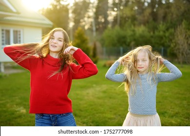 Two Cute Sisters Fooling Around Together On The Grass On A Sunny Summer Day. Children Being Silly And Having Fun. Family Time.