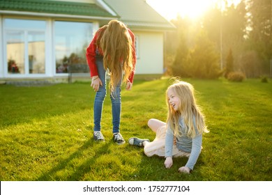 Two Cute Sisters Fooling Around Together On The Grass On A Sunny Summer Day. Children Being Silly And Having Fun. Family Time.