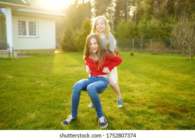 Two Cute Sisters Fooling Around Together On The Grass On A Sunny Summer Day. Children Being Silly And Having Fun. Family Time.