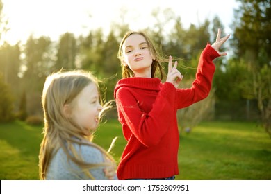 Two Cute Sisters Fooling Around Together On The Grass On A Sunny Summer Day. Children Being Silly And Having Fun. Family Time.