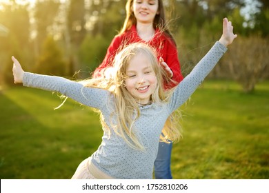 Two Cute Sisters Fooling Around Together On The Grass On A Sunny Summer Day. Children Being Silly And Having Fun. Family Time.