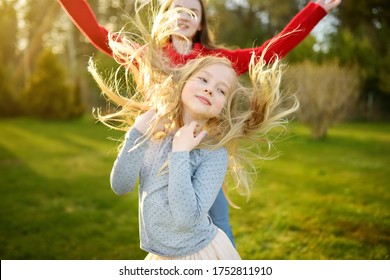 Two Cute Sisters Fooling Around Together On The Grass On A Sunny Summer Day. Children Being Silly And Having Fun. Family Time.