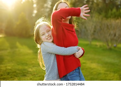 Two Cute Sisters Fooling Around Together On The Grass On A Sunny Summer Day. Children Being Silly And Having Fun. Family Time.