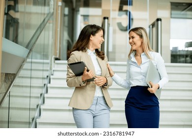 Two cute young business women walking on stairs in the office hallway - Powered by Shutterstock