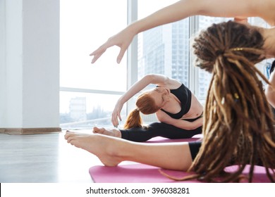 Two Cute Young Woman Stretching On The Floor In Yoga Center Together