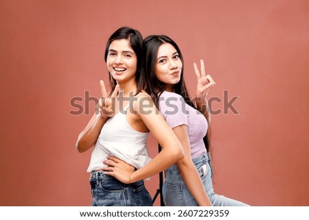 Two cuties are standing back-to-back posing for the camera and making a peace sign