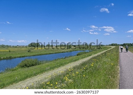 Two cyclists cycle on a dike along the Waal river