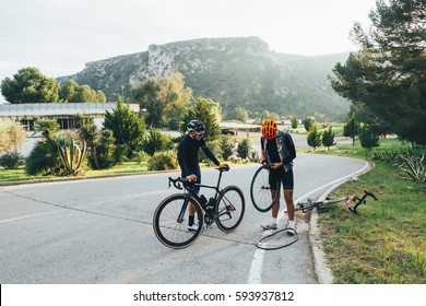 Two Cyclists Fixing A Flat Tire On The Side Of The Road In The Soft Light
