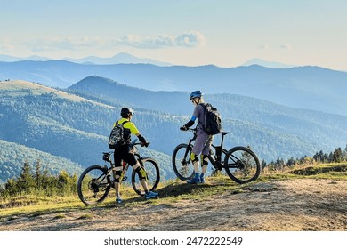 Two cyclists men riding electric bikes outdoors. Back view of male tourists resting on the top of hill, enjoying beautiful mountain landscape, wearing helmet and backpack. Concept of active leisure. - Powered by Shutterstock