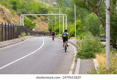 Two Cyclists Riding Down a Winding Road in a Green Valley - Powered by Shutterstock