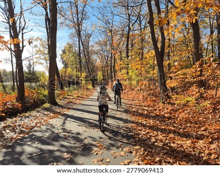 Two cyclists riding through vibrant autumn forest path — family active lifestyle, fall season outdoor activity