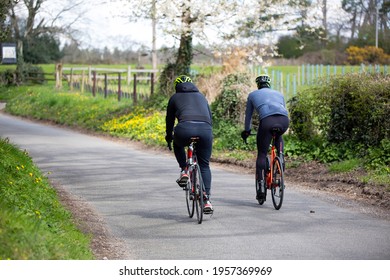 Two Cyclists Riding Together On An English Countryside Road