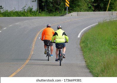 Two cyclists wear bright, reflective clothing on a two lane road to create high visibility awareness for motorists. 