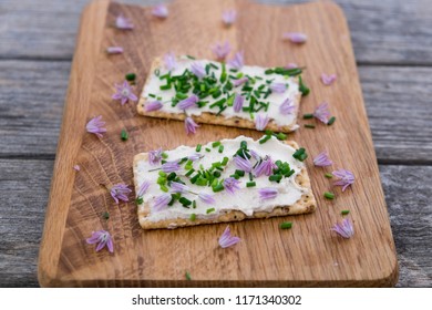 Two Dairy And Lactose-free Vegan Cream Cheese Spread Made From Cashew And Macadamia Nuts On Crackers With  Chopped Chives And Edible Chive Flowers On Wooden Chopping Board With Shallow Depth Of Field