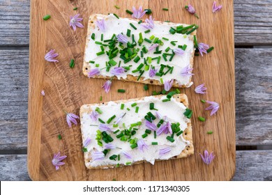 Two Dairy And Lactose-free Vegan Cream Cheese Spread Made From Cashew And Macadamia Nuts On Crackers With Fresh Chopped Chives And Edible Chive Flowers On A Wooden Chopping Board