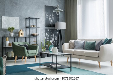 Two dark posters hanging on a grey wall in industrial living room interior with lamps, bright couch and table standing on a carpet