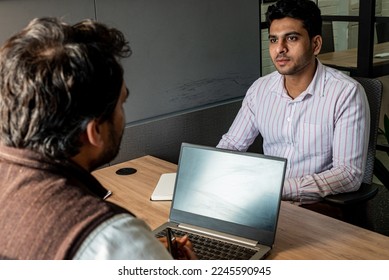 Two dark-haired Indian colleagues, dressed in traditional formal office attire, converse with one another in an official meeting while seated together in a corner office during the daytime in Delhi. - Powered by Shutterstock