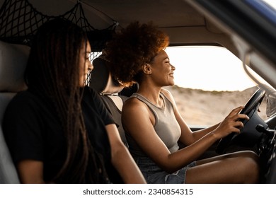 Two dark-skinned girls are driving a camper van to go on vacation. The woman with the afro hair drives the car while the girl with the braided hair is the co-pilot.Travel to the mountain. - Powered by Shutterstock