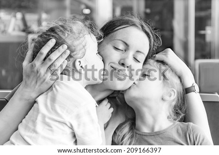 Two daughters kissing their happy mother