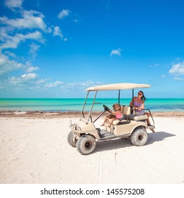 two daughters and their mother driving golf cart at tropical beach