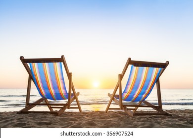 Two Deck Chairs On A Tropical Sandy Beach With Beautiful Colorful Sunset