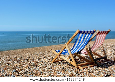 two deckchairs on a pebbled beach, facing out to sea