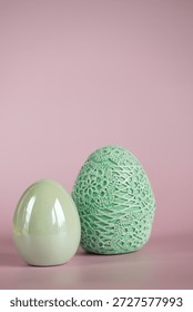 Two decorative Easter eggs in shades of green on a pink background. Minimalistic composition, spring mood, the concept of the Easter holiday.