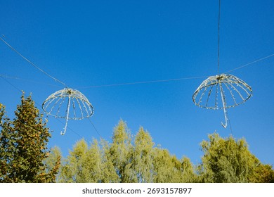 Two decorative umbrella frames with lights hang in the air over trees.