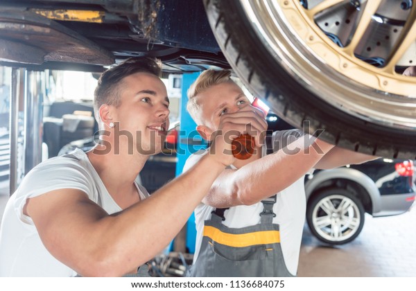 Two dedicated auto mechanics tuning a car through\
the modification of the rims, while working together in a modern\
automobile repair shop