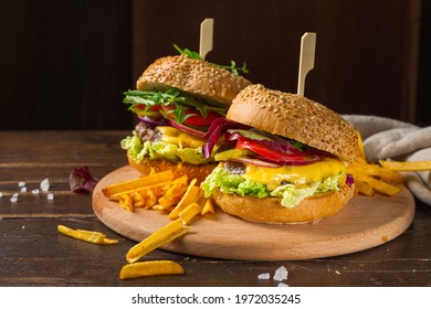 Two delicious burgers with mixed salad, cucumbers and tomatoes on a wooden round tray. Dark wooden background, horizontal frame, rustic