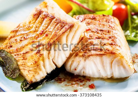 Two delicious fillets of marinated grilled or oven baked pollock or coalfish served with a fresh salad, close up view showing the texture