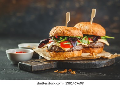 Two Delicious Homemade Burger With Beef, Tomatoes, Cheese, Arugula And Chard On A Wooden Cutting Board. Street Food, Fast Food.