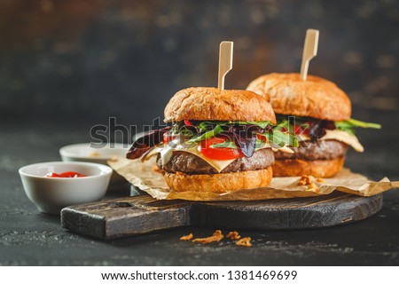 Two delicious homemade burger with beef, tomatoes, cheese, arugula and chard on a wooden cutting board. Street food, fast food.