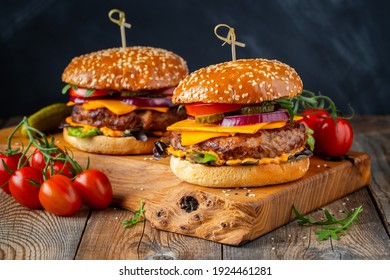 Two delicious homemade burgers of beef, cheese and vegetables on an old wooden table. Fat unhealthy food close-up.
