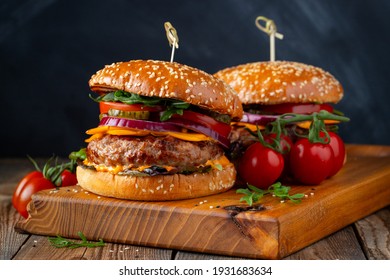 Two delicious homemade burgers of beef, cheese and vegetables on an old wooden table. Fat unhealthy food close-up