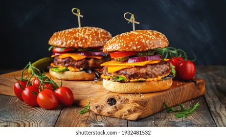 Two delicious homemade burgers of beef, cheese and vegetables on an old wooden table. Fat unhealthy food close-up