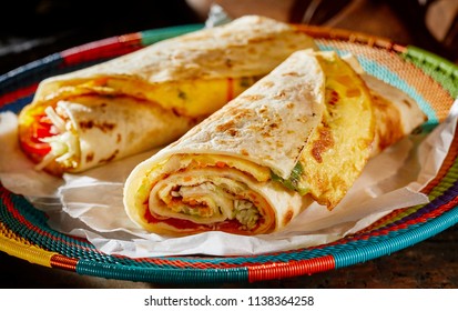 Two delicious indigenous Ugandan Rolex Rolls made with egg omelette and diced fresh vegetables rolled in a chapati or roti on a colorful woven basket