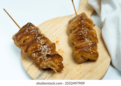 Two delicious skewers of puff pastry topped with sesame seeds displayed on a wooden board. Perfect for appetizers, snacks, or party food, showcasing golden-brown flaky texture and savory taste - Powered by Shutterstock